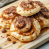 Stack of golden-brown, extra-fluffy pancakes drizzled with cinnamon-sugar syrup and topped with a swirl of cream cheese frosting, fresh blueberries, and finely chopped pecans on a rustic wooden board, with soft natural light and light steam rising.