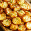 Golden parmesan potatoes with a crispy parmesan crust, garnished with chopped parsley and lemon zest, served on a rustic wooden board.