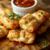 Golden brown crispy cheese sticks with bubbling mozzarella center, arranged on a wooden board with a small bowl of marinara, sprinkled with Parmesan and parsley for a rustic family-friendly presentation.