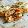 Golden-brown crispy pizza hot pockets on a light wooden board, one pocket sliced open to reveal melty mozzarella, diced chicken, and bright marinara filling. The crust shows a slight blister, with a dusting of oregano and a few fresh basil leaves for color. Served with a small bowl of marinara and parchment paper peeking from the edge.